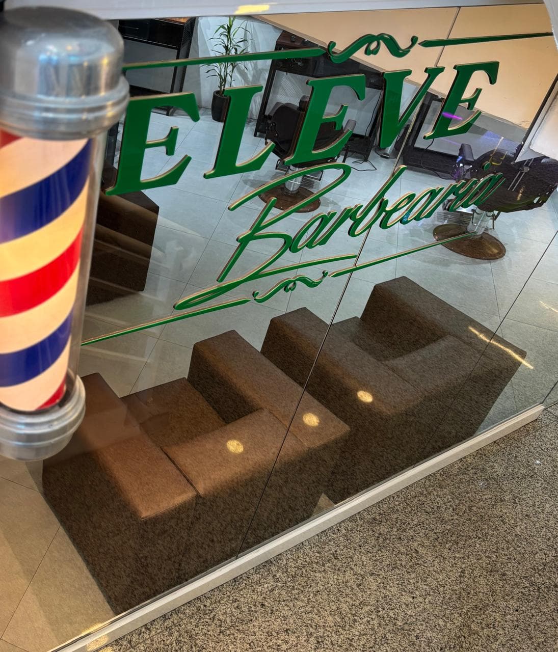 Vitrine de vidro da Eleve com a marca aplicada e o poste de barbeiro ao lado